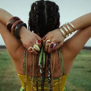Rear view of a woman in a yellow dress with braided hair adorned with colorful rings and bracelets.