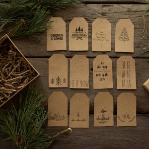Flat lay of handmade eco-friendly Christmas tags on wooden surface with pine sprigs.