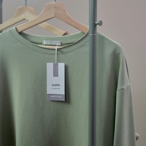 Close-up of a green shirt on a hanger with label tag on a minimalist clothing rack.