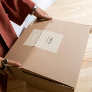 Close-up of a woman packing a cardboard box on a wooden table indoors.